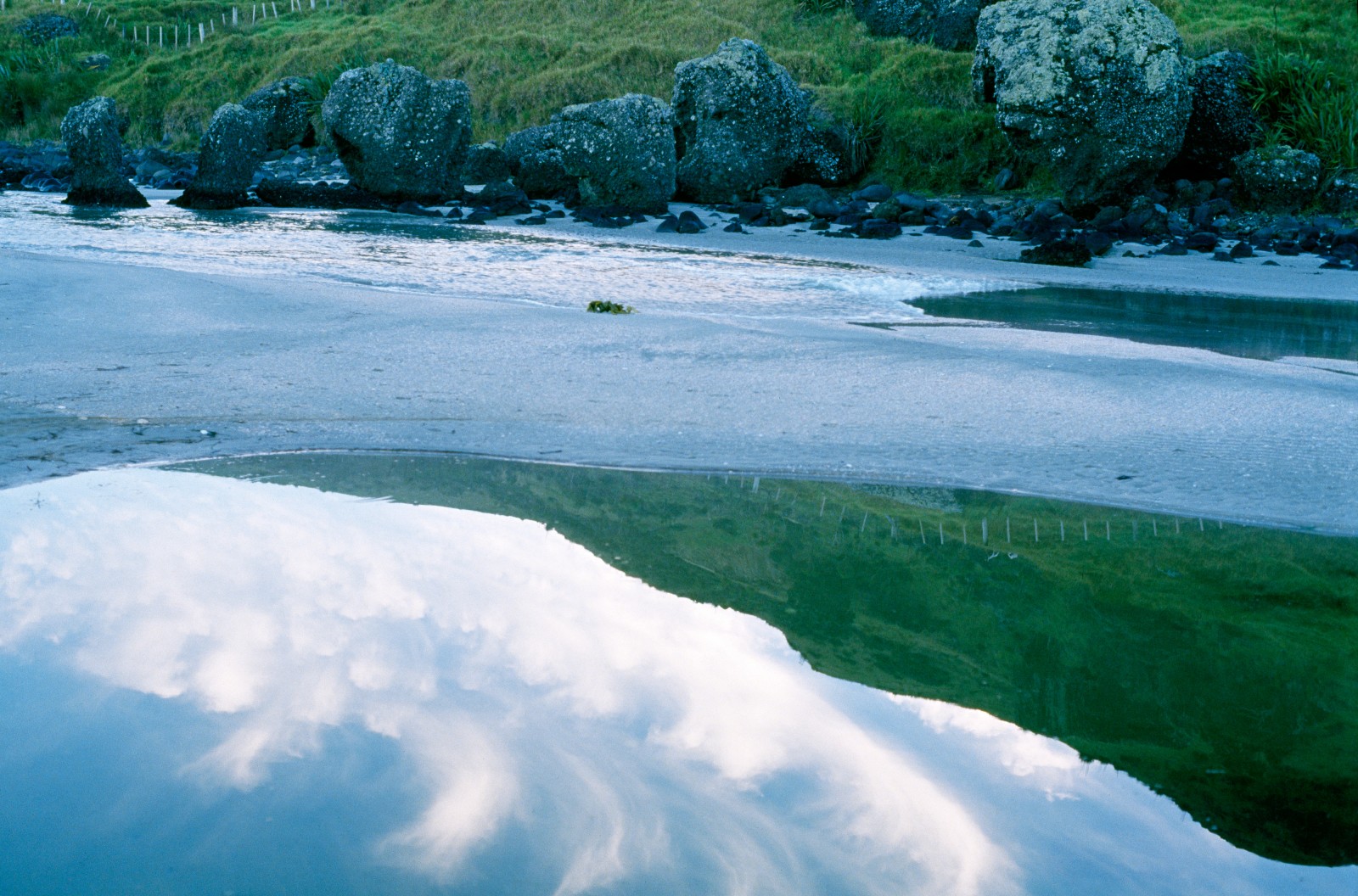 04_Spirit'sFlight_08 Tohe named this beach Te Horo (walk fast) because of its quicksand; sacred Maori burial ground at Spirits Bay is reflected in the waters of the tidal estuary. At top of picture are work stones which were used by the Maori for shaping tools.